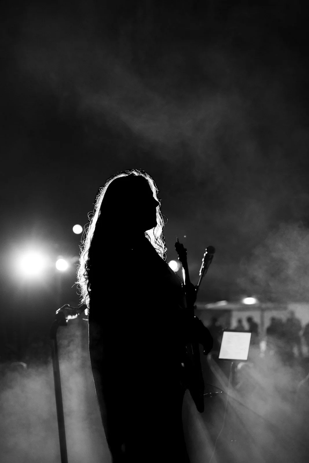 Silhouette einer Frau mit E-Gitarre bei einem Konzert in Schwarz-Weiß, im Hintergrund surrende Beleuchtung.