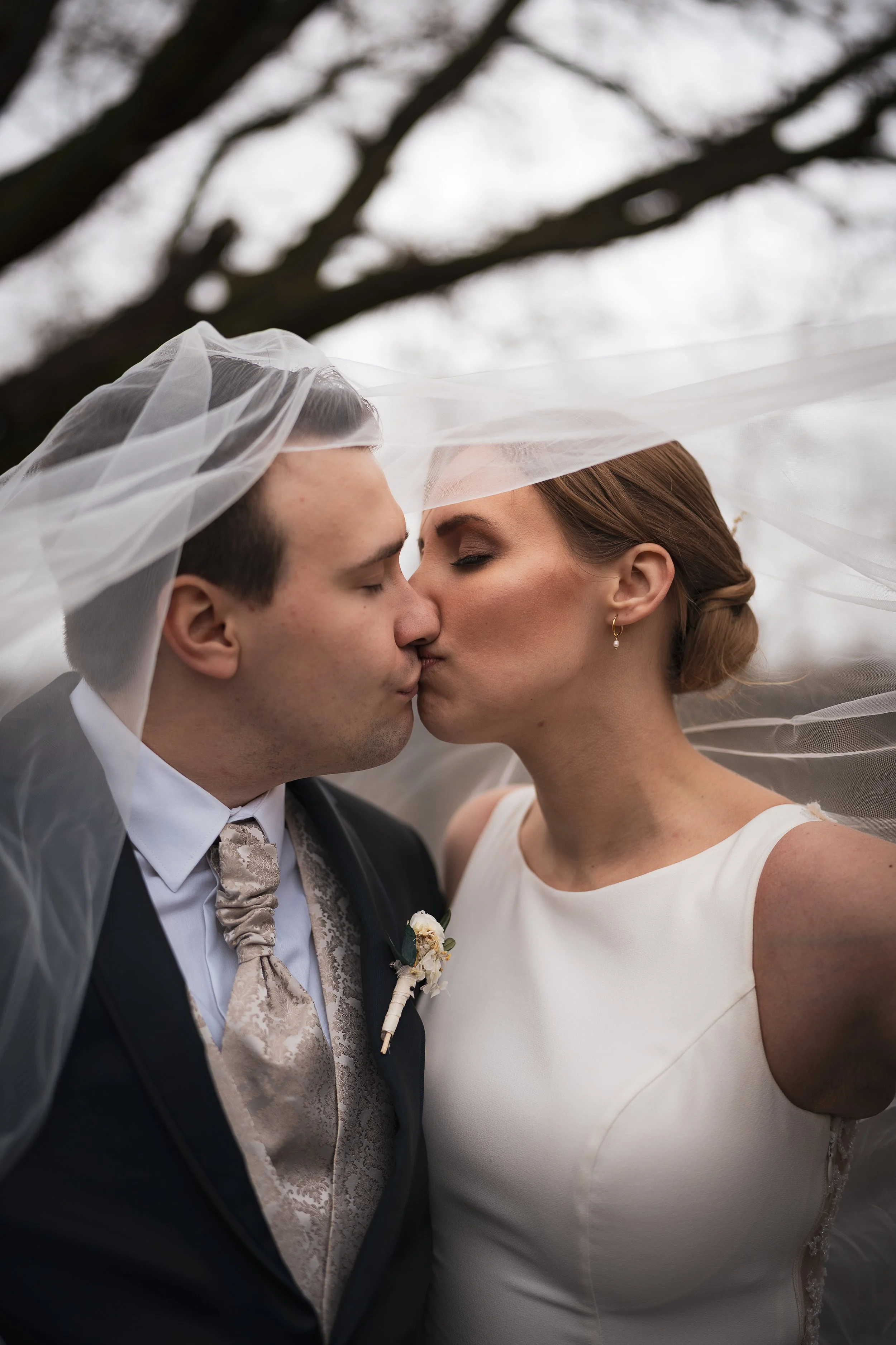 Ein Brautpaar küsst sich unter einem Schleier bei einer Hochzeit im Freien.