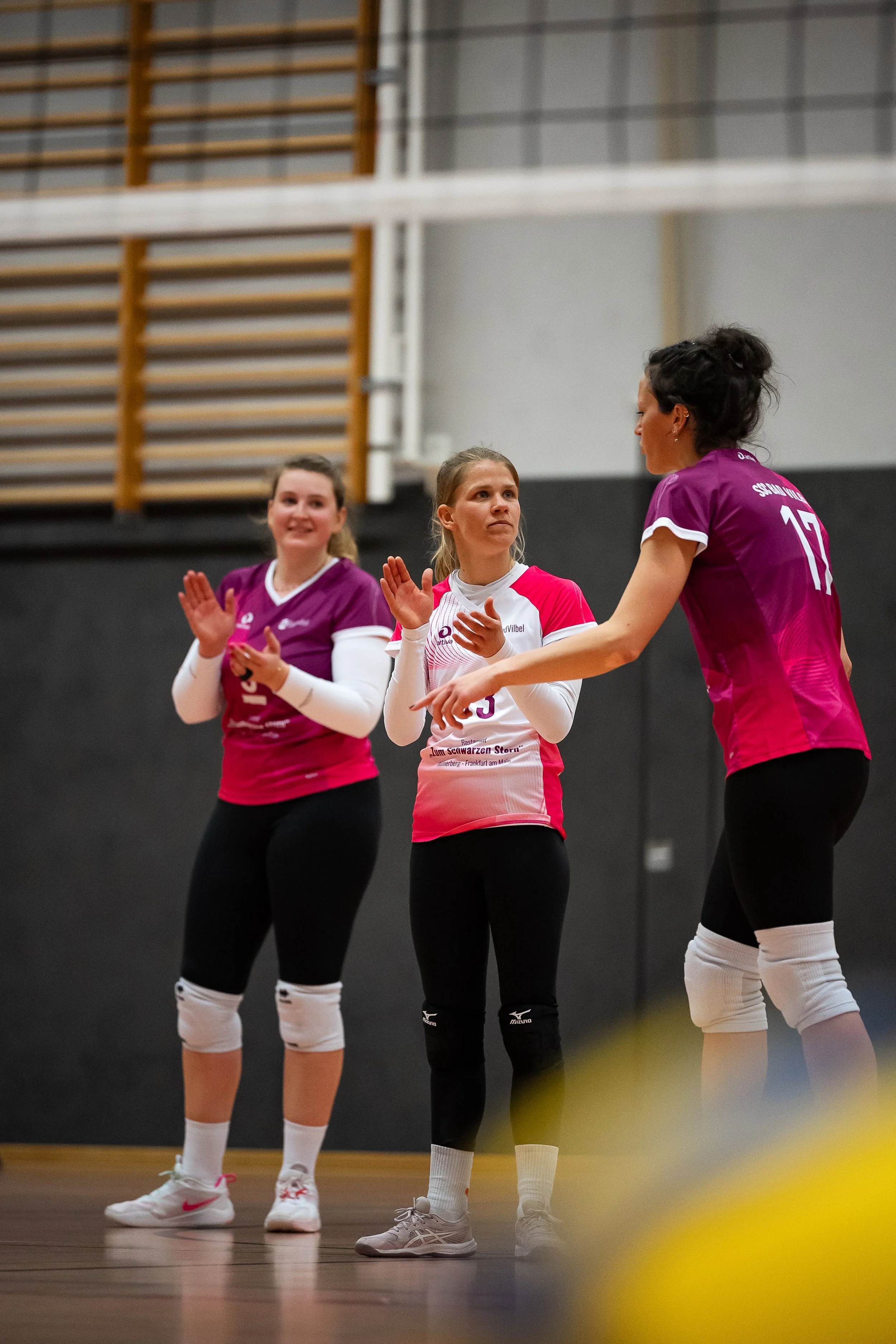 Drei weibliche Volleyballspielerinnen in einem Indoor-Sporthalle, die sich unterhalten, während sie in Volleyball-Union-Uniformen gekleidet sind.