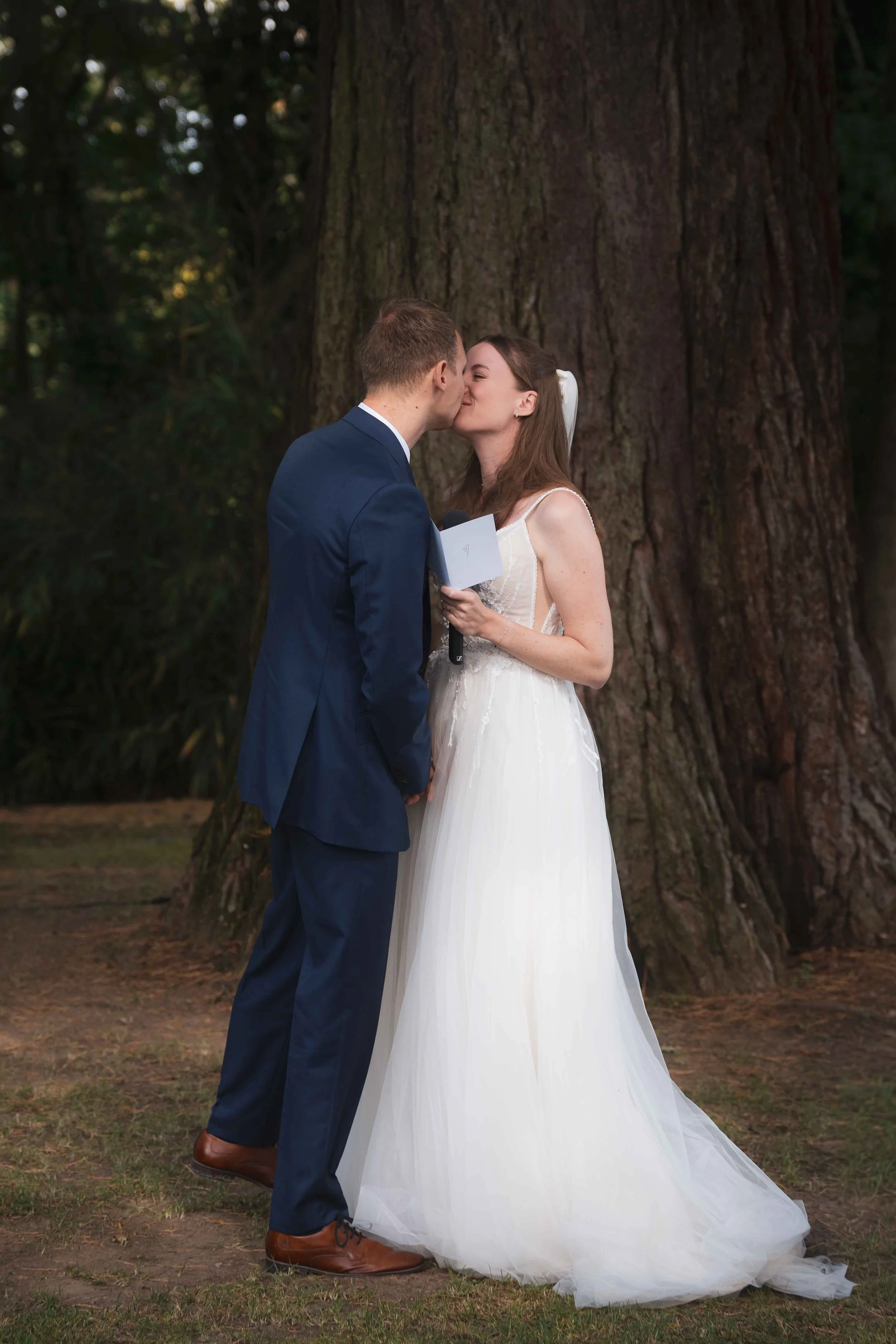 Ein Brautpaar bei einer Hochzeit, das sich vor einem Baum küsst.