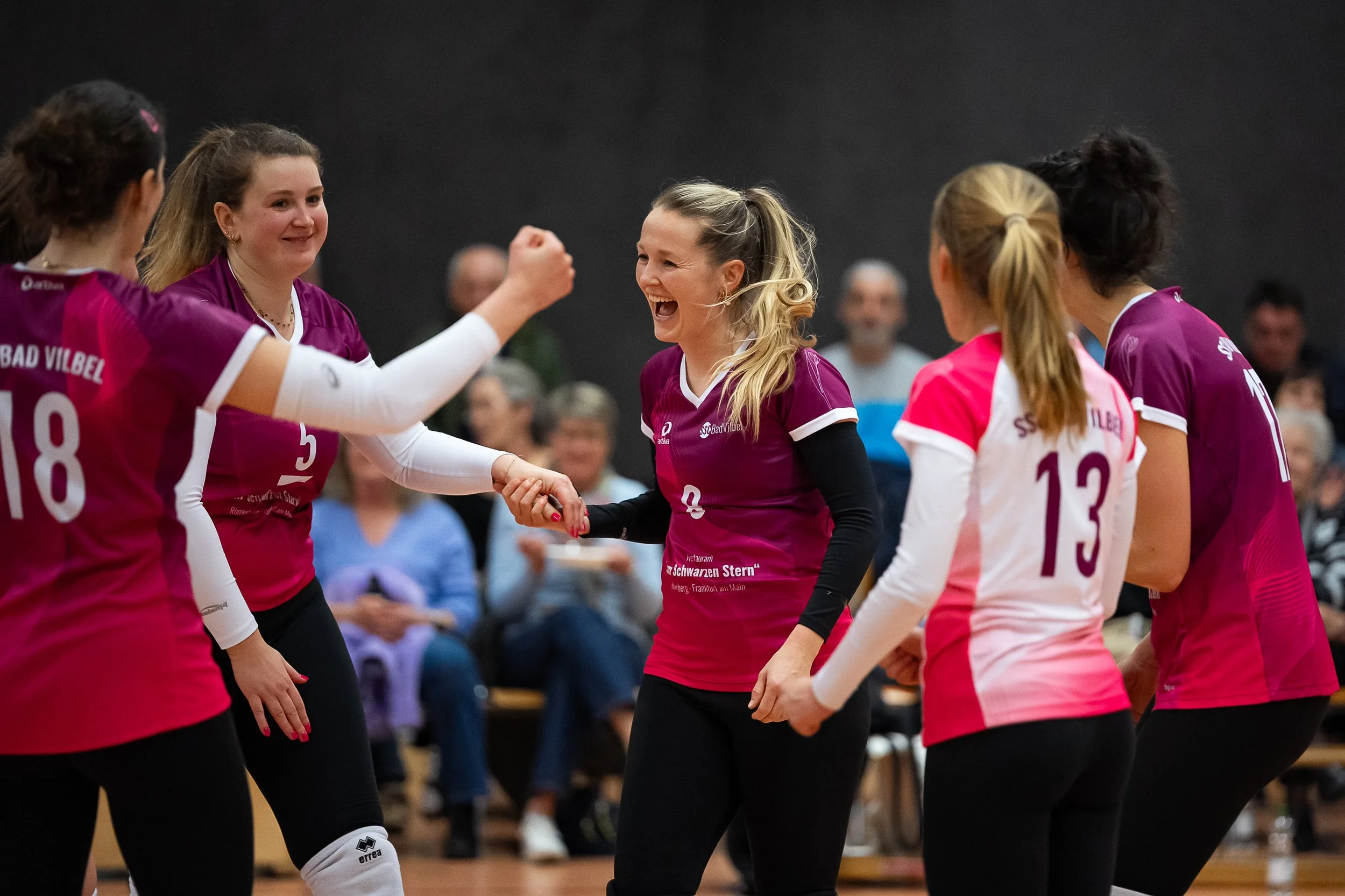 Frauen im Volleyball tragen pink und weiß Trikots, feiern und schütteln sich die Hände während eines Spiels.