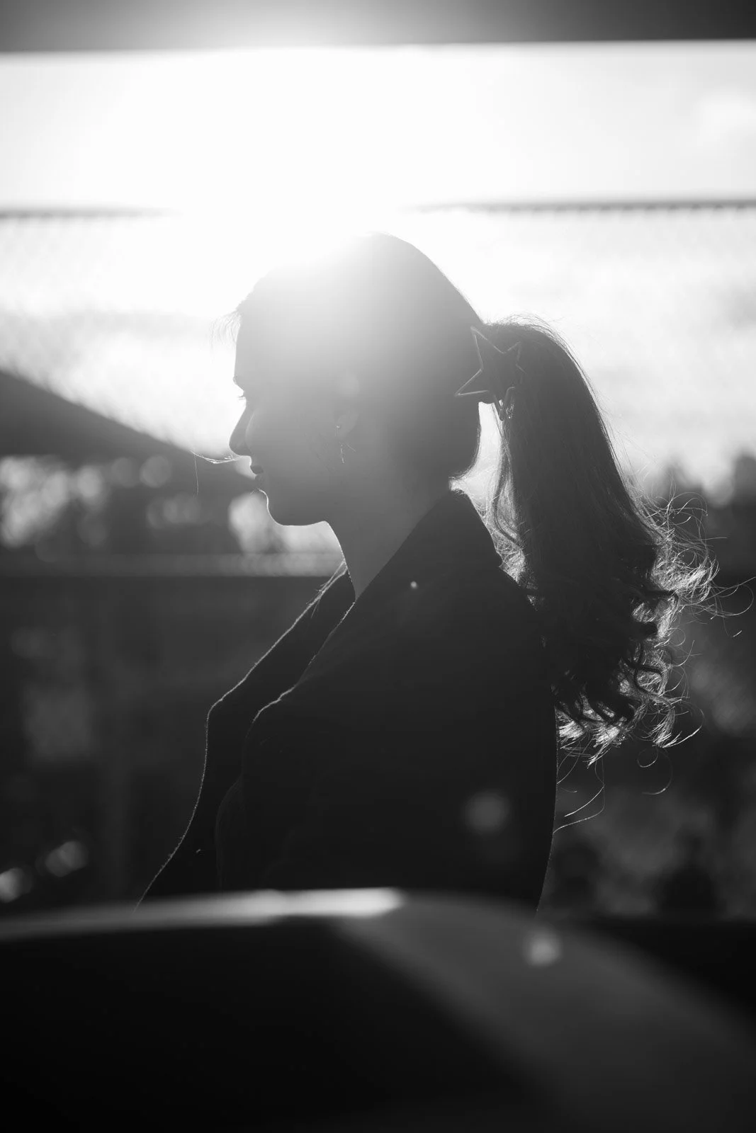 Schwarz-weiß-Foto einer Frau im Profil, mit einem Haargummi und Stern-Ohrring, Sonnenlicht im Hintergrund.