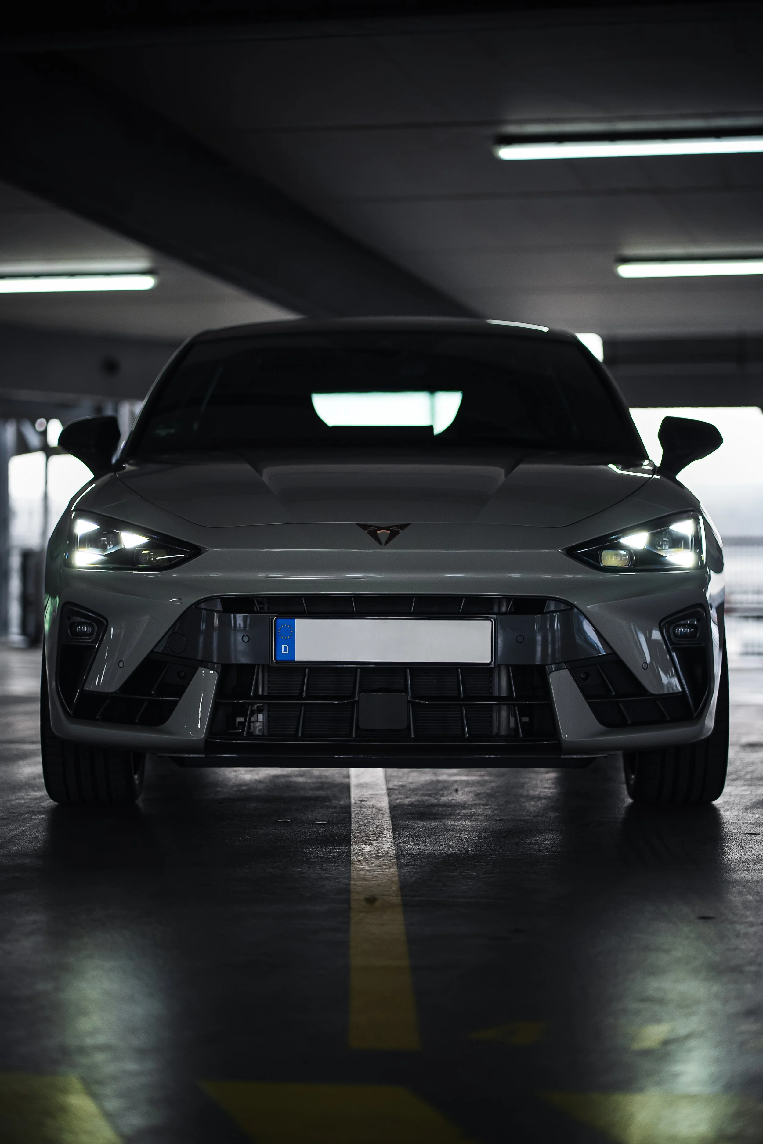 Ein graues Auto in einem Parkhaus, frontal fotografiert, mit dunklem Hintergrund und Deckenbeleuchtung.