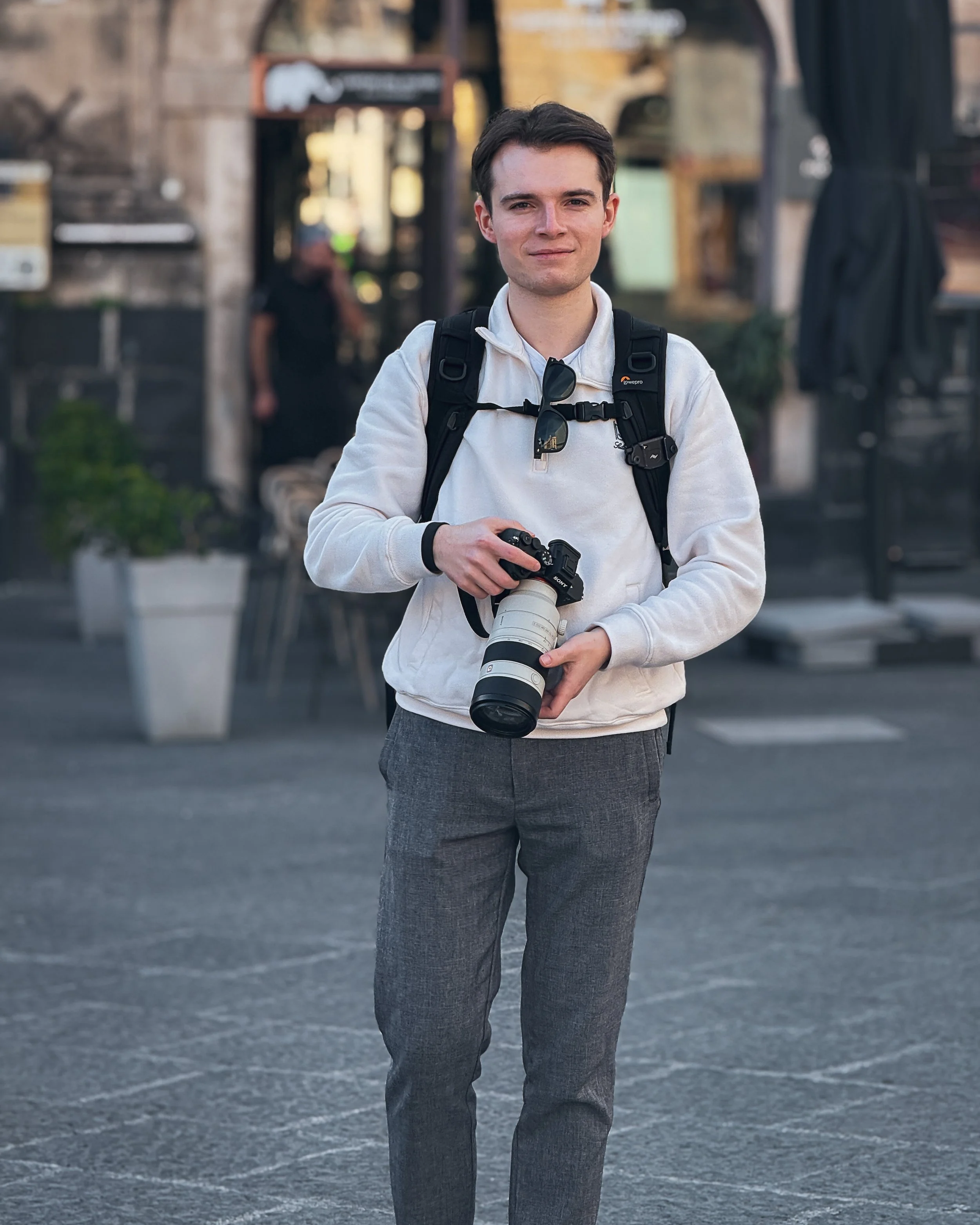 Junge Mann mit Rucksack und Kamera auf der Straße in einer Stadt.