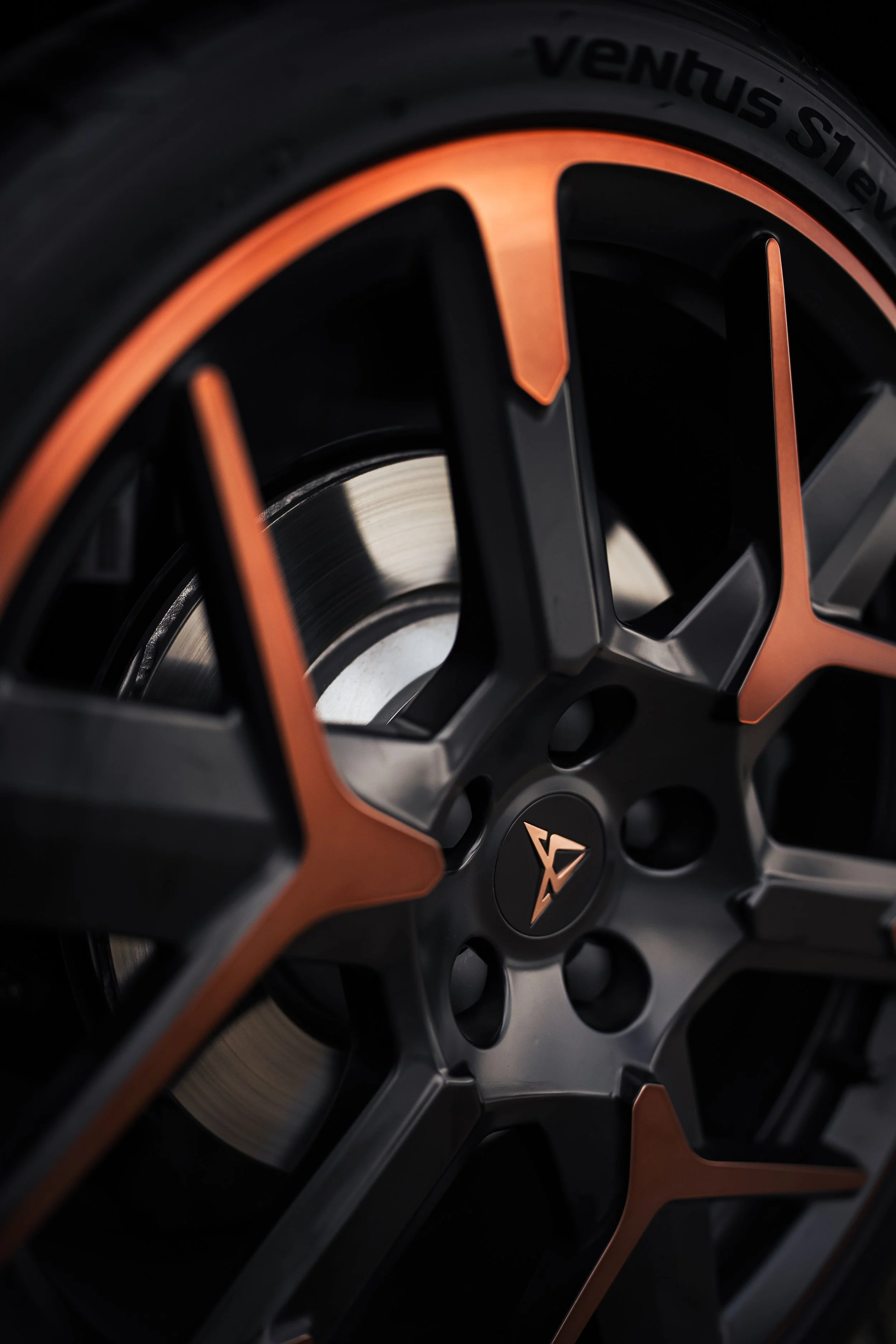 Nahaufnahme eines Autoreifens und Felgens mit schwarzem und kupferfarbenem Design, das Markenlogo ist sichtbar.