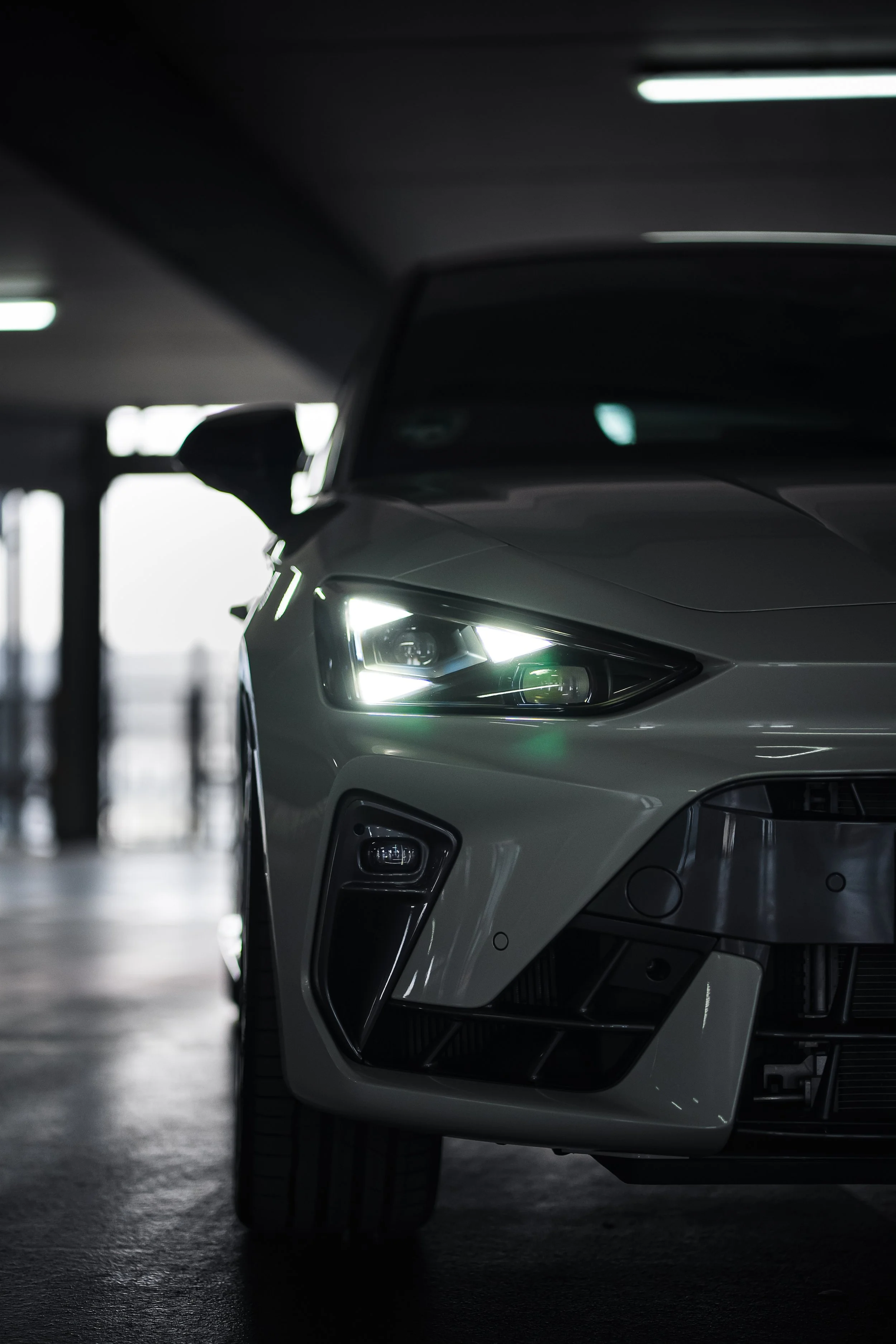 Nahaufnahme eines weißen Autos, seitlicher Blick, in einer dunklen, indoor Umgebung, mit leuchtenden Scheinwerfern.