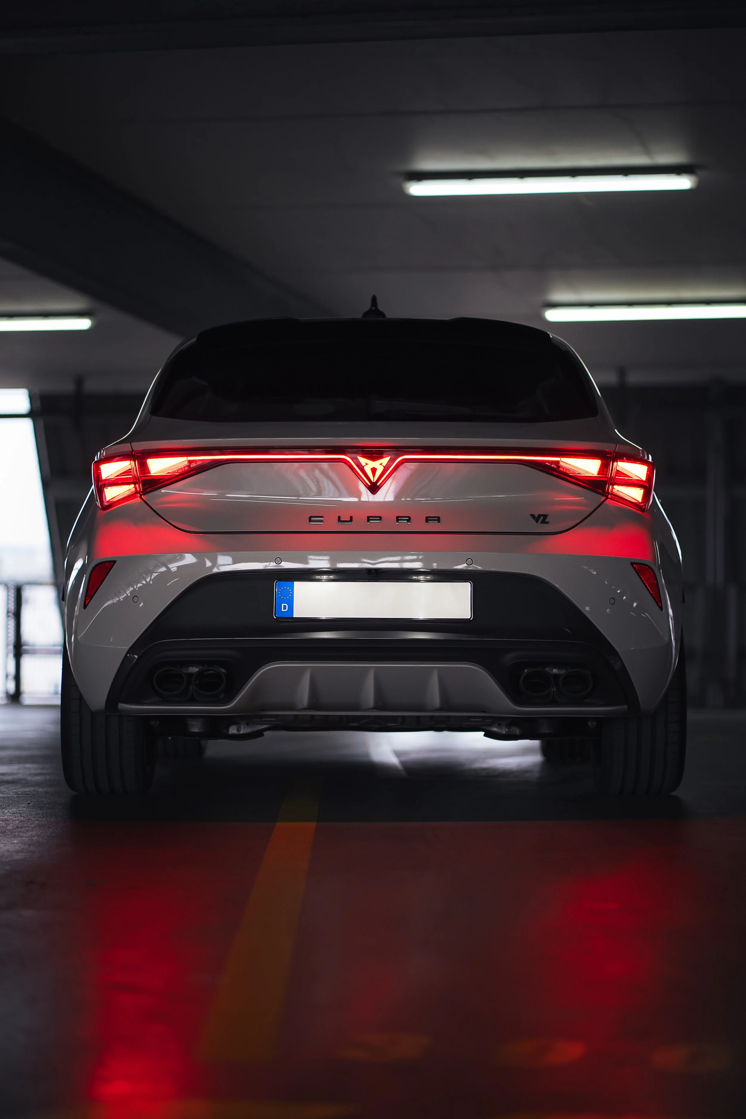 Rückansicht eines weißen CUPRA VZ Autos in einer Tiefgarage, beleuchtet von Deckenlampen.