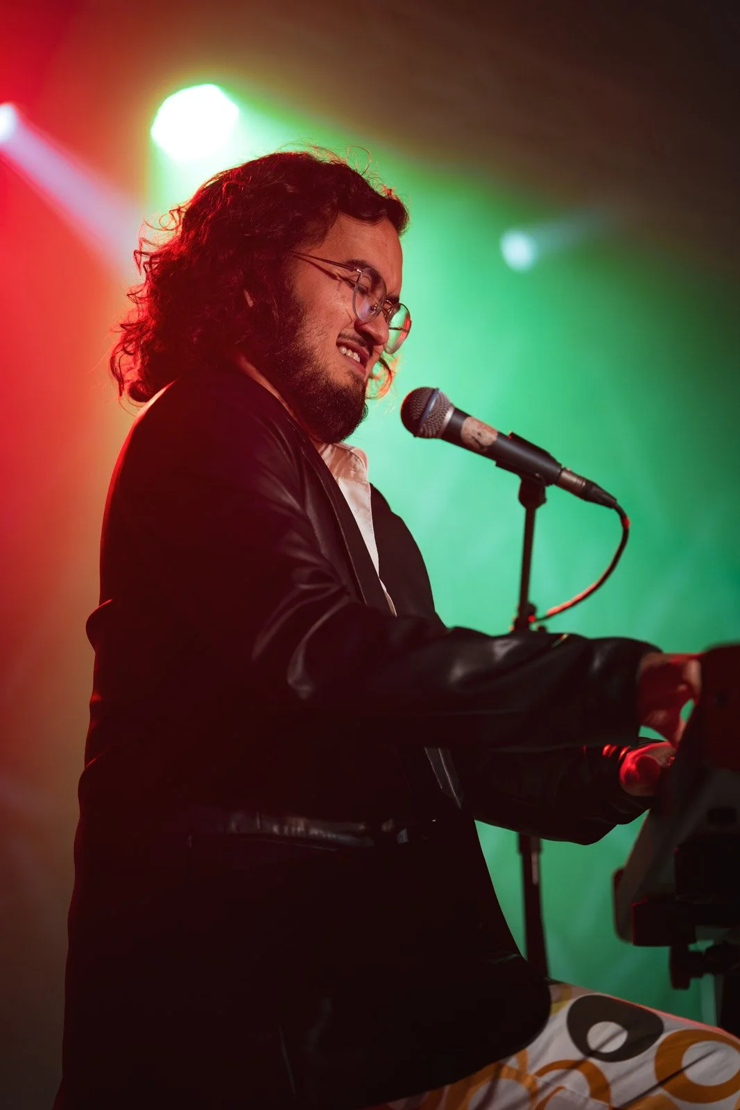Ein männlicher Musiker spielt auf einem Keyboard auf einer Bühne, hinter ihm leuchten bunte Scheinwerfer, die grün, rot und Weiß sind.