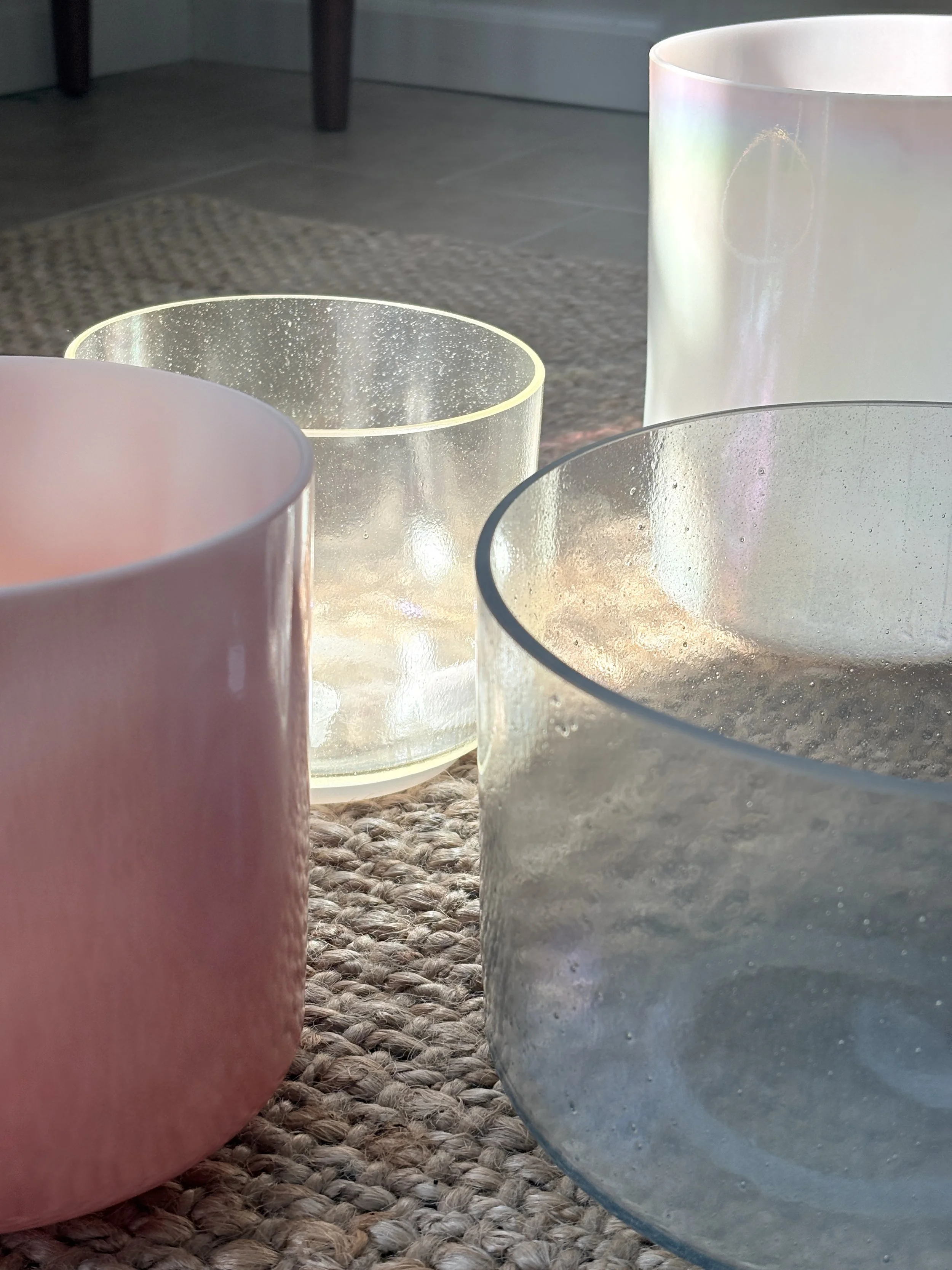 Close-up image of four iridescent glass candle holders on a woven mat, with a door and floor in the background.