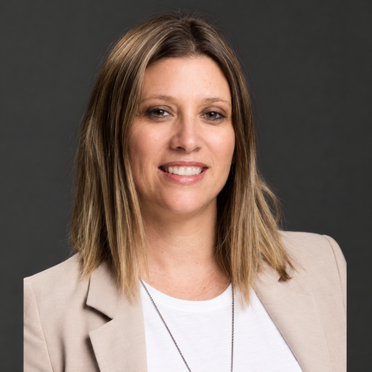 Professional woman with shoulder-length light brown hair, wearing a beige blazer and white shirt, smiling against a dark background.