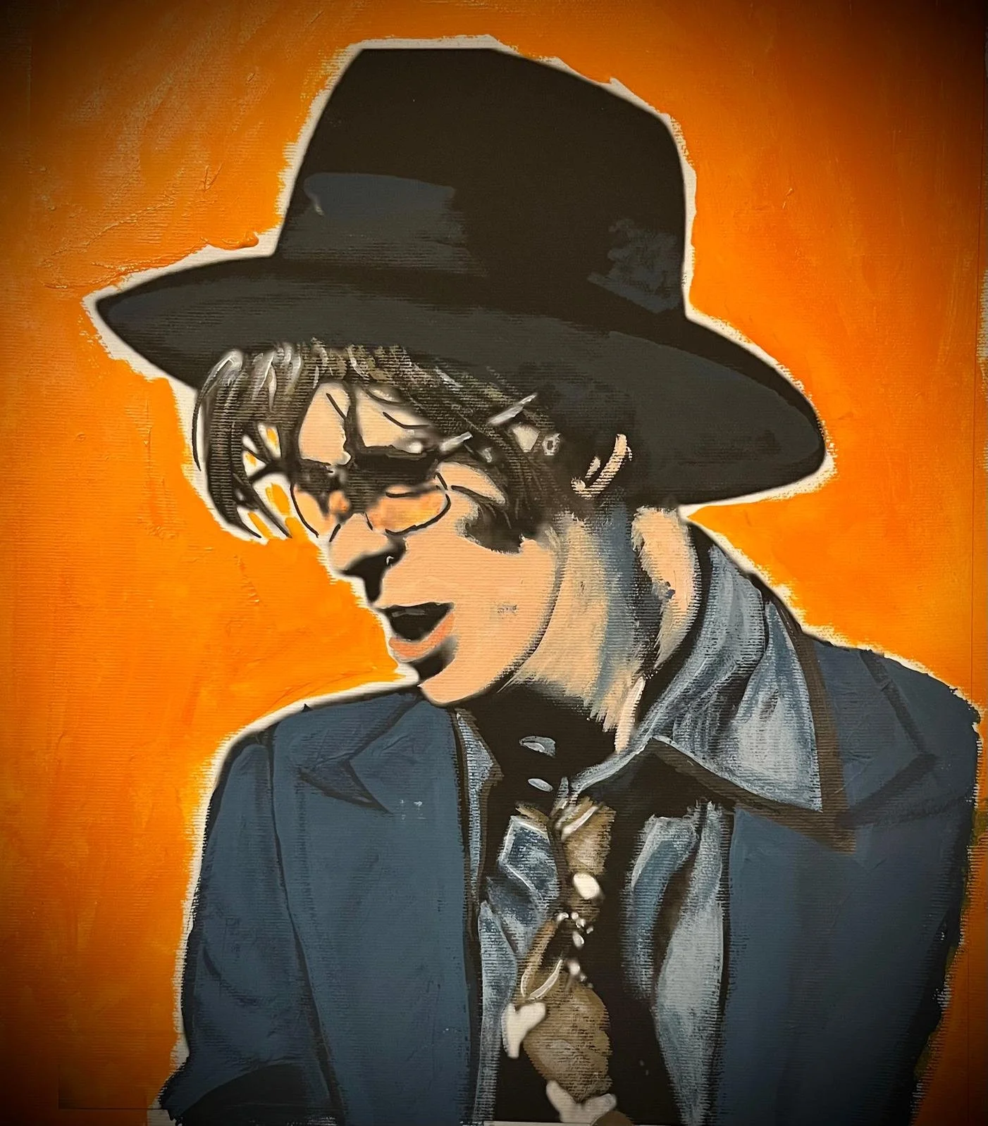 Portrait of a woman in a wide-brimmed black hat, sunglasses, a collared shirt, and a blazer, against an orange background.
