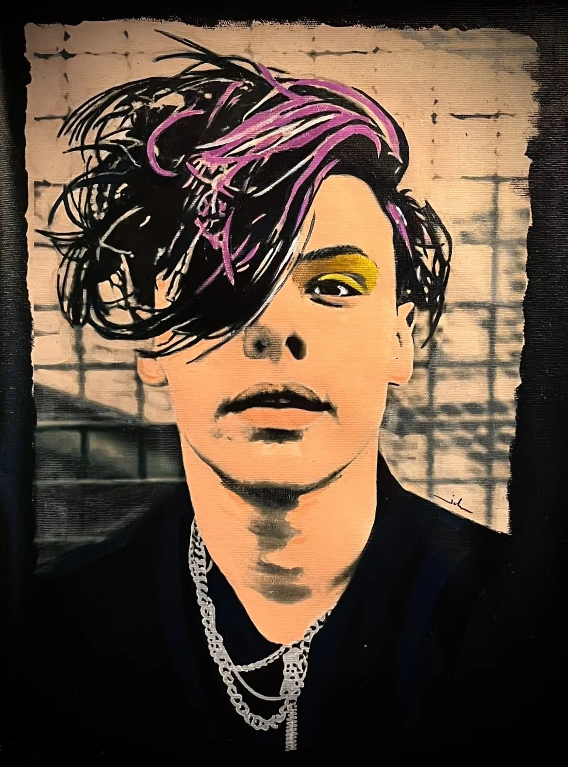 A portrait of a person with short, tousled black hair with purple highlights, one eye covered by the hair, wearing bright yellow eyeshadow and black lipstick, adorned with chains around the neck. The background features a brick wall.