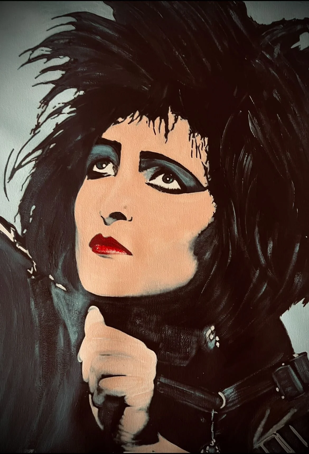 Painting of a woman with spiky black hair, heavy blue eye makeup, red lipstick, and a black leather jacket, holding her hand near her chin.