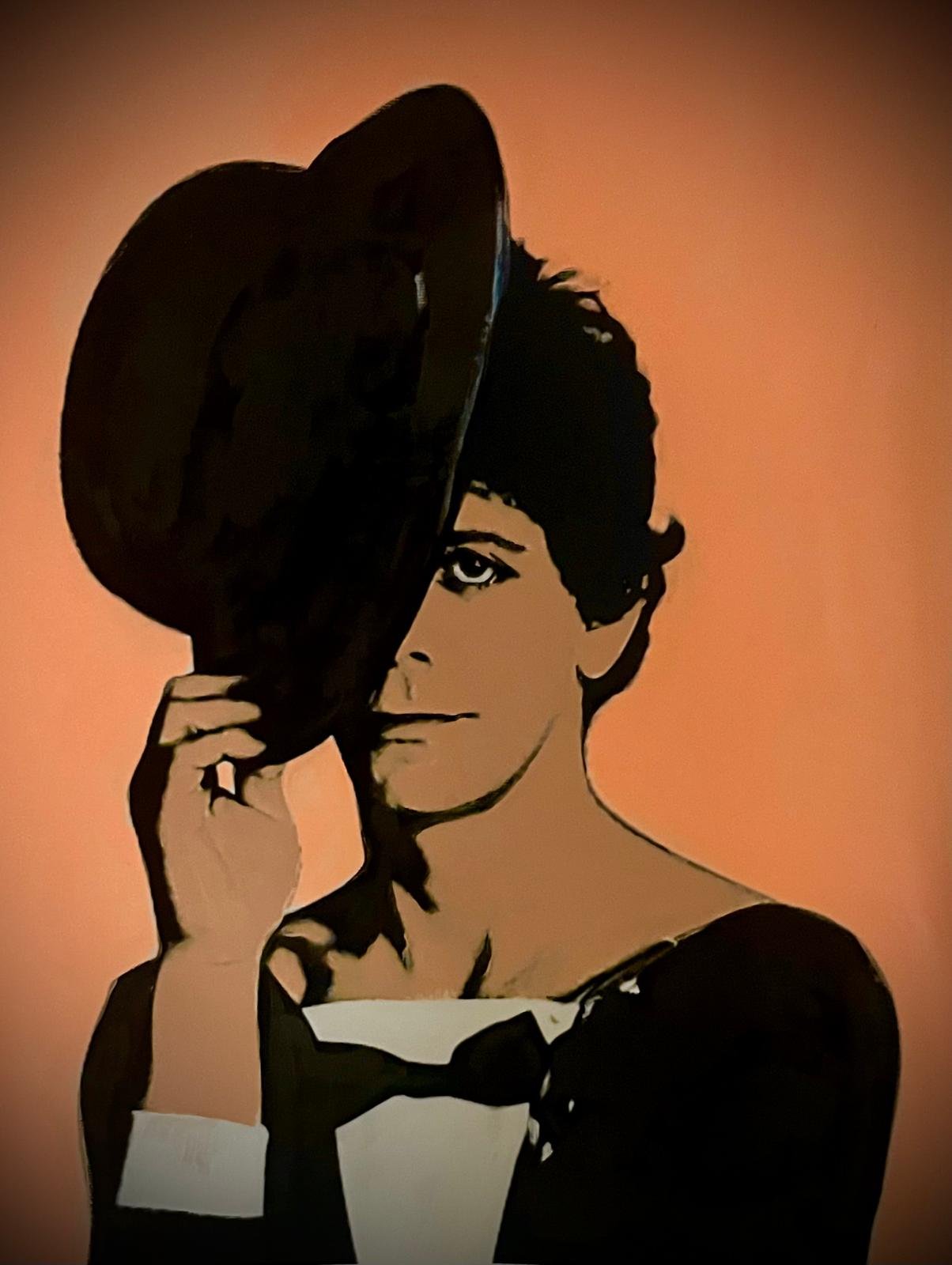 A digital illustration of a woman with short hair, holding a black hat over part of her face while looking at the viewer, with a warm orange background.