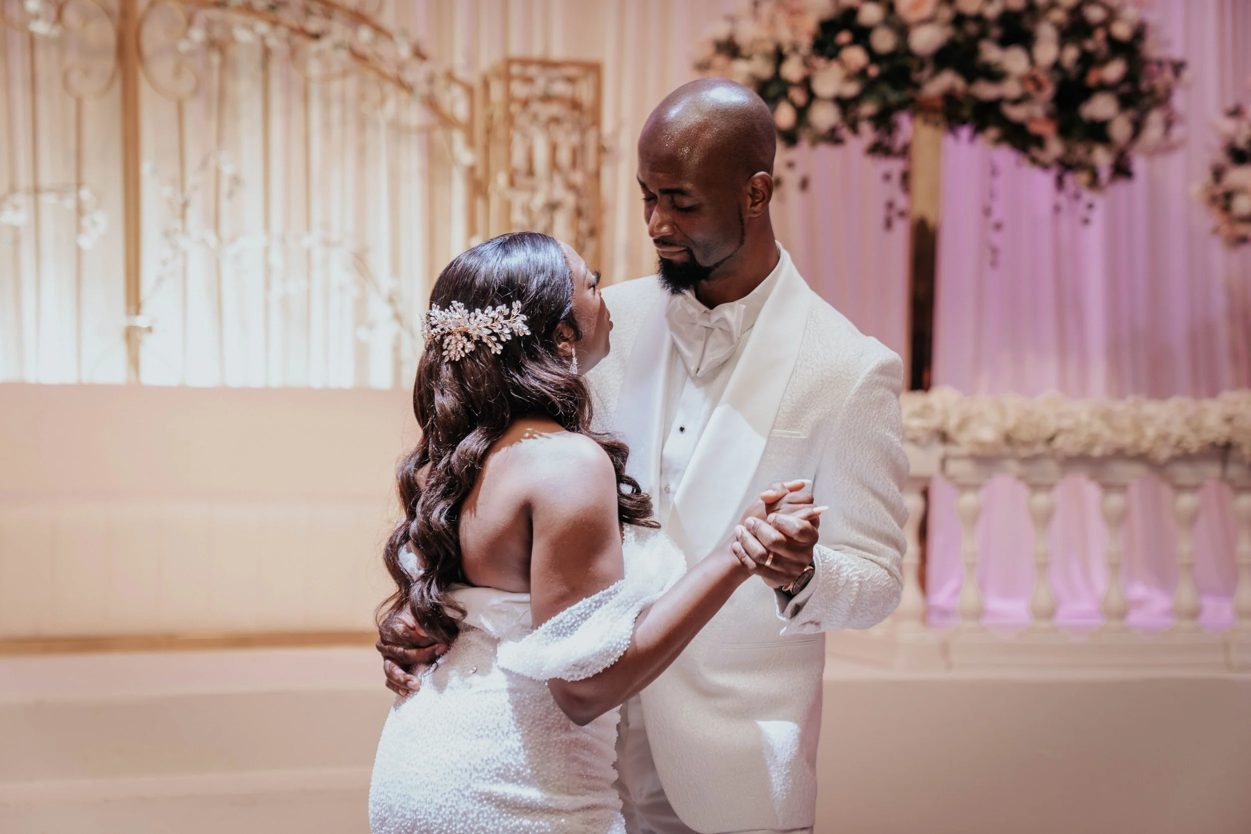 Een bruid en bruidegom dansen samen op een huwelijksfeest, omgeven door bloemstukken en zachte verlichting.