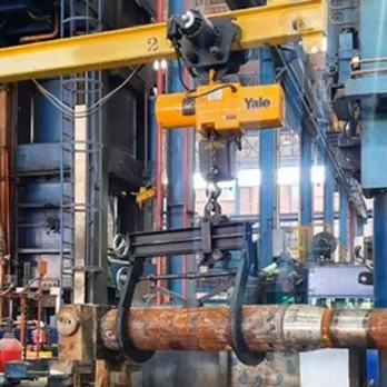 Un robot de grúa Yale levantando un tubo de metal en un entorno industrial.