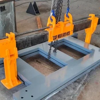 Estructura metálica gris en una superficie de trabajo, con un sistema de sujeción amarillo y negro para levantarla, y cadenas negras conectadas a ganchos amarillos, todo en un espacio industrial.