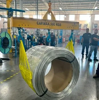 Un rollo grande de metal en un almacén con maquinaria y personas alrededor.