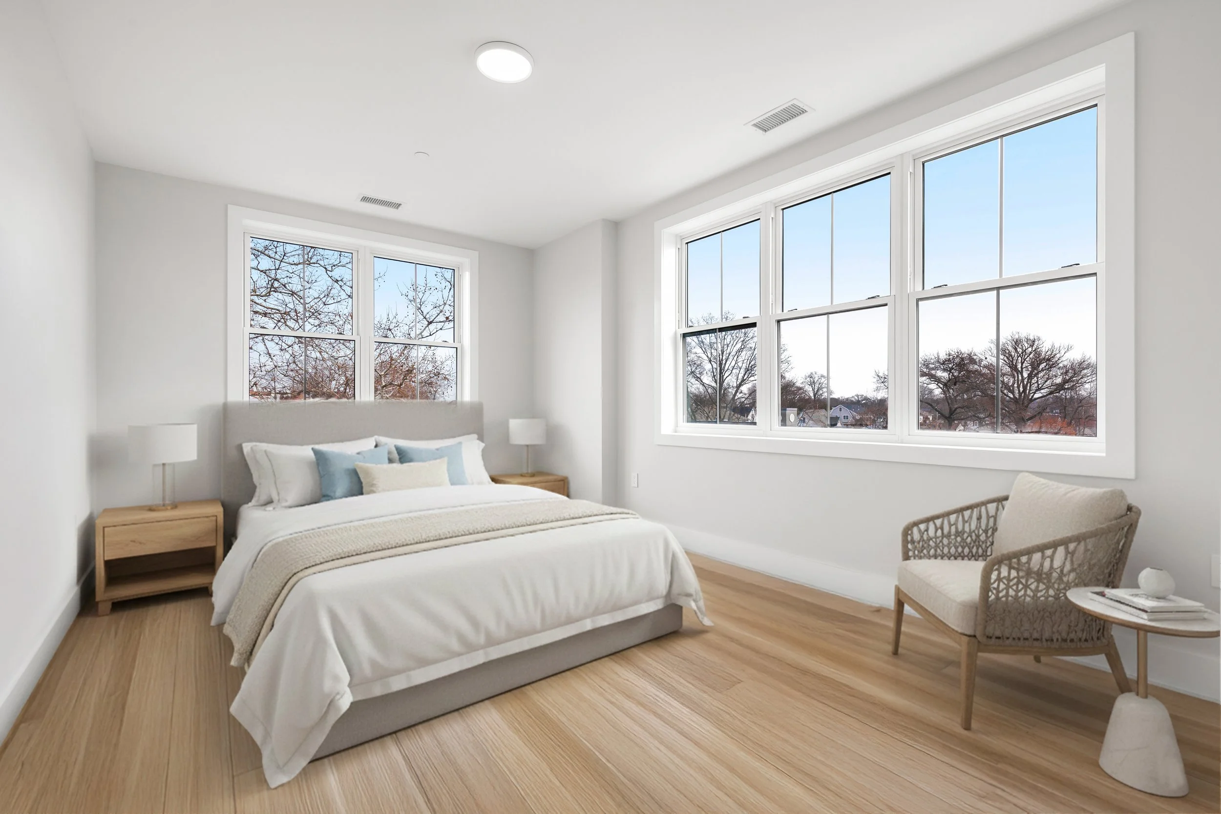 A minimalist bedroom with a bed, wooden nightstands, lamps, a cozy chair, and large windows showing an outdoor winter scene.