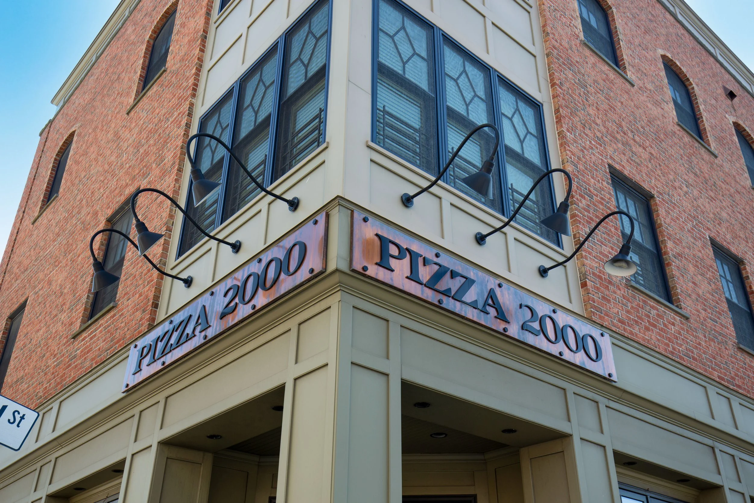 Corner of a building with a sign that reads 'PIZZA 2000' and exterior lights above the sign.