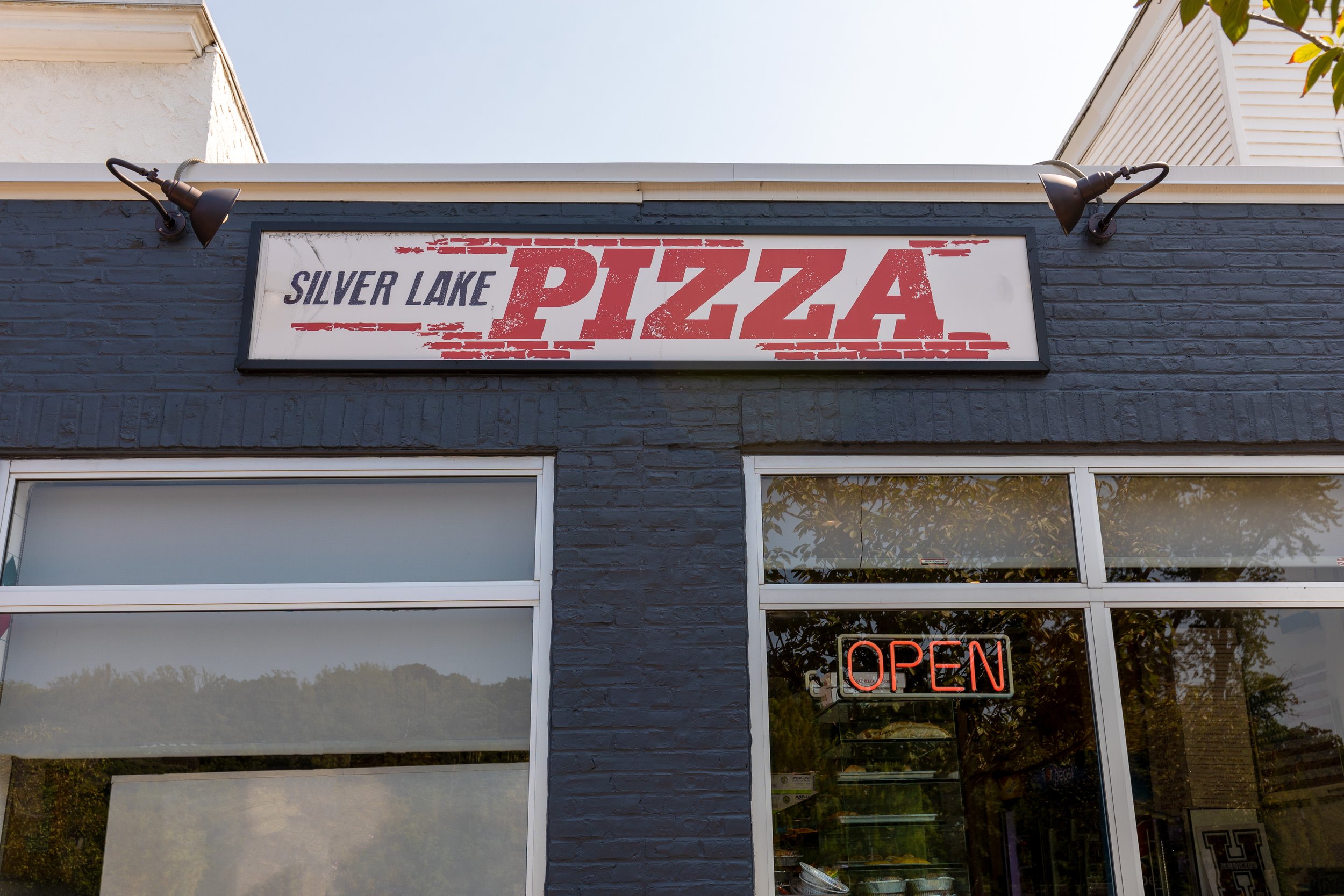 Front of a pizza restaurant named Silver Lake Pizza with a sign displaying the name, and a neon sign in the window indicating the restaurant is open.