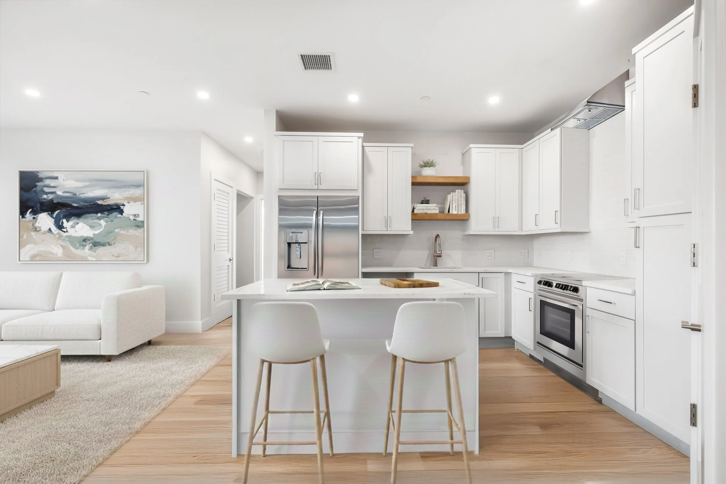 Modern white kitchen with island, stainless steel appliances, open shelving, and light wood flooring, adjacent to a living room with a white sofa and artwork.