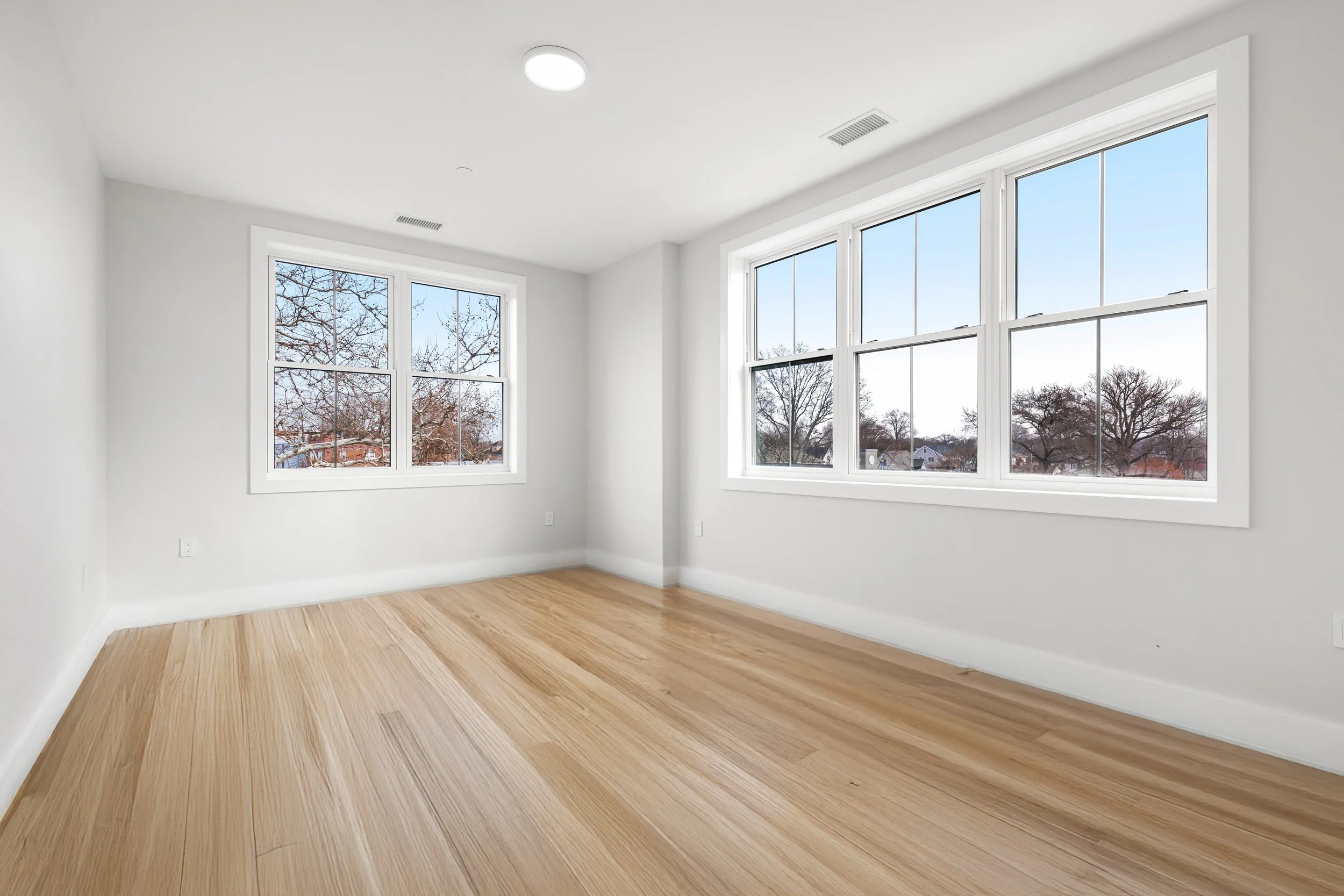 Empty room with white walls, large windows, and wooden floor.