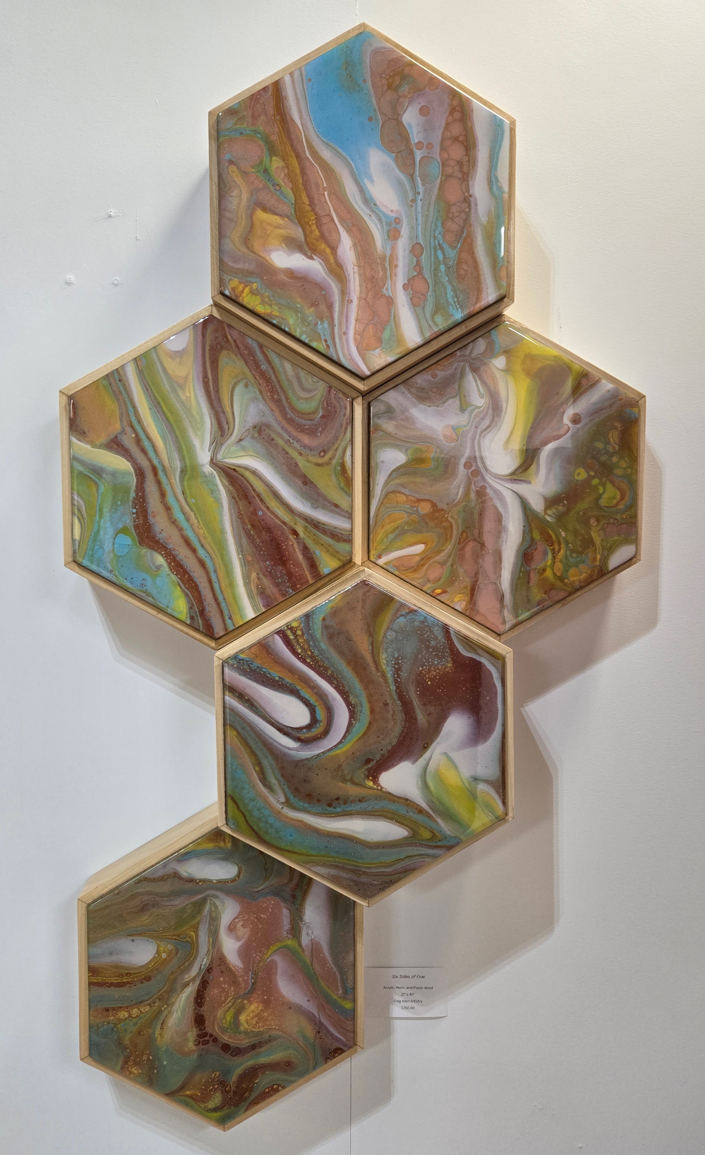 Five hexagonal acrylic and resin art pieces with colorful swirling patterns, arranged in a vertical staggered display on a white wall.