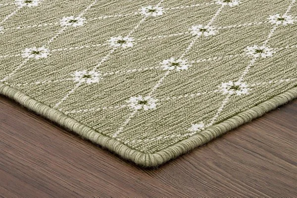 Close-up of a green rug with a white floral pattern on a wooden floor.