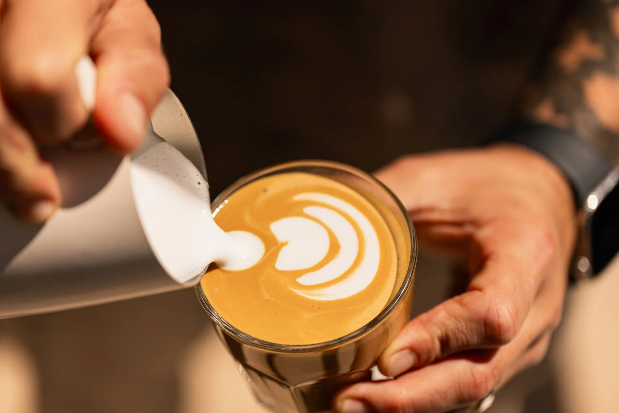 Person pouring steamed milk into a cup of espresso to create latte art.