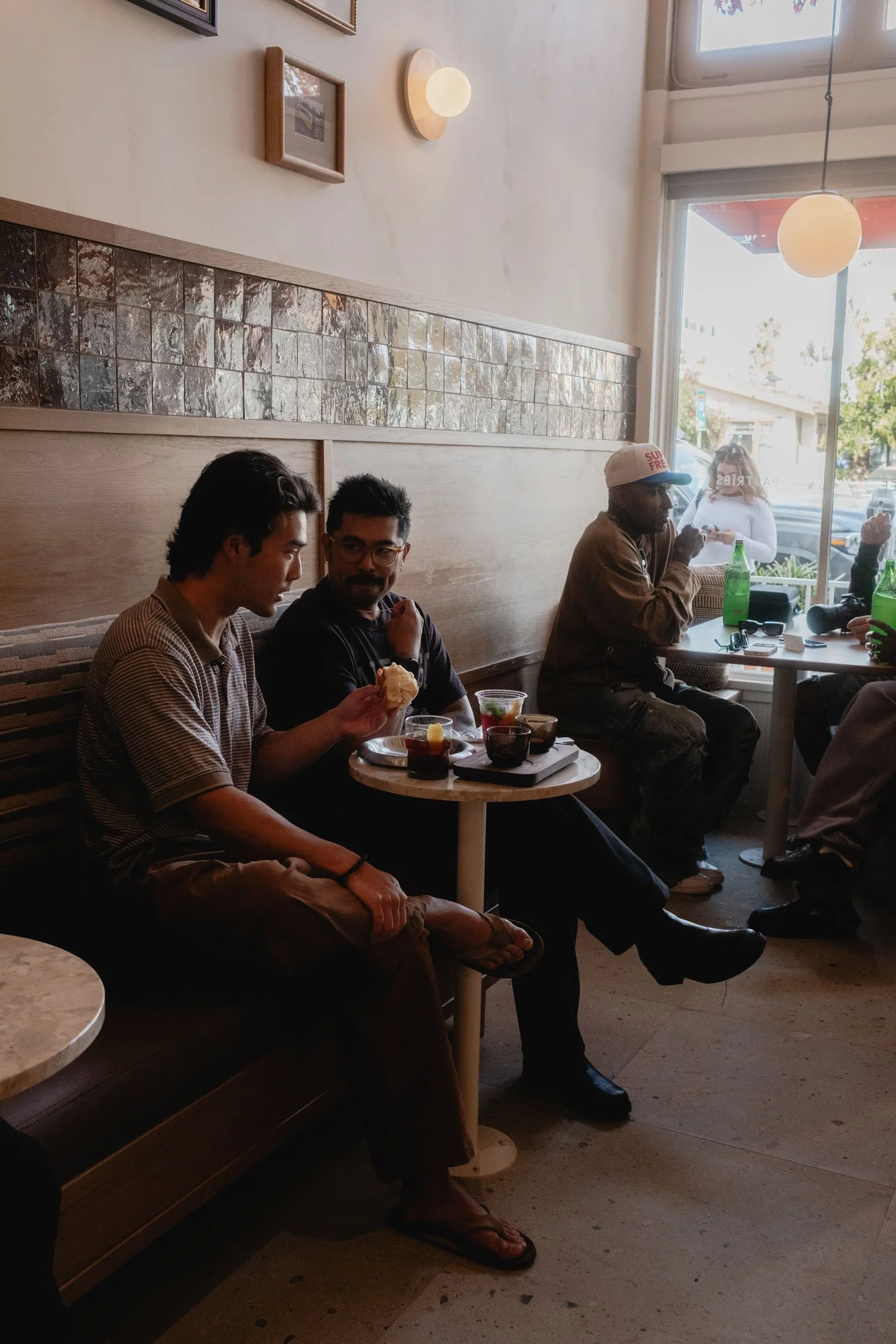 Three men sitting at a small table in a cafe or restaurant, with drinks and food, engaging in conversation. 