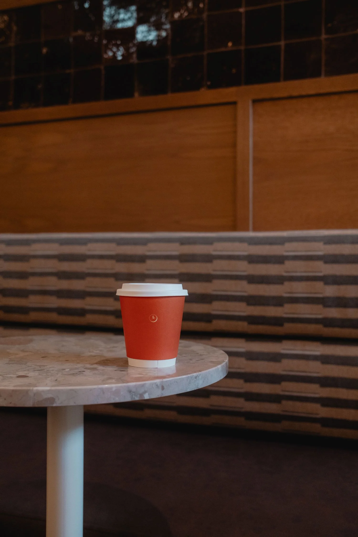 An orange to-go coffee cup with a white lid on a small round marble table.