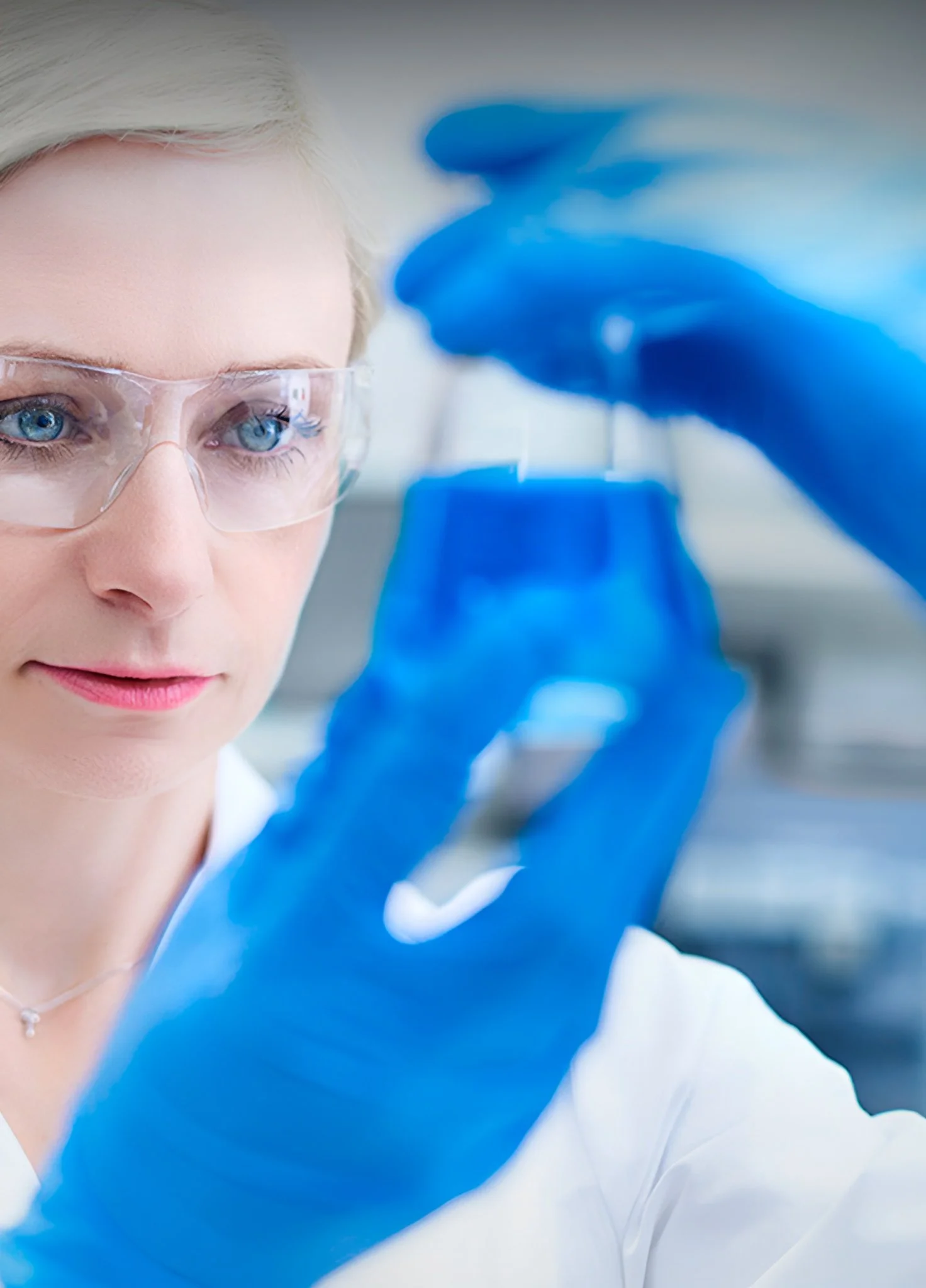 A scientist wearing safety goggles and blue gloves examines a laboratory sample in a controlled environment.