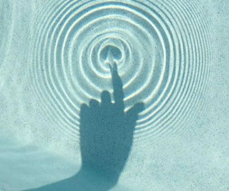 Shadow of a hand with an extended middle finger creating ripple-like shadows on a textured surface.