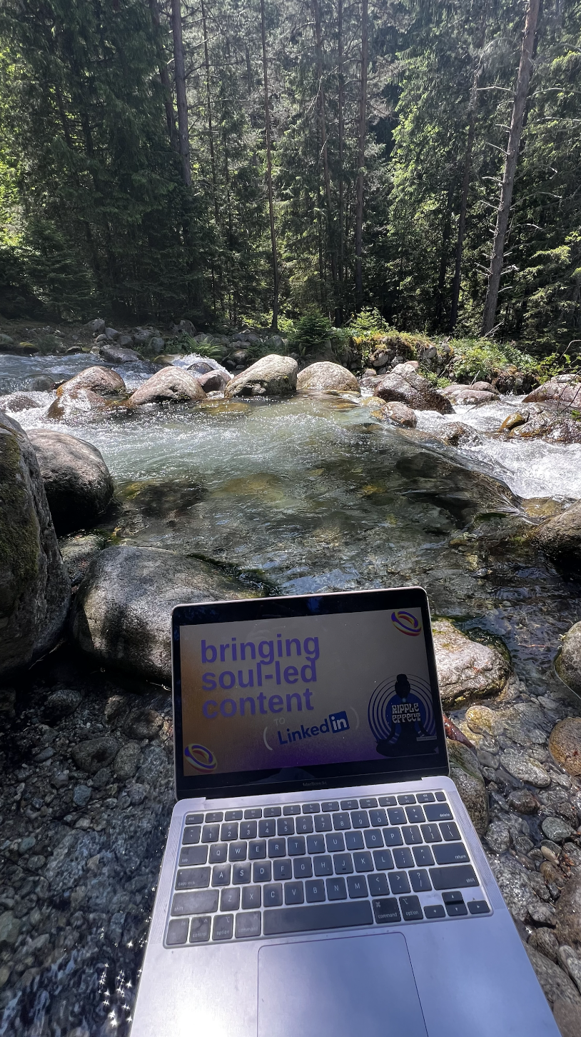 A laptop on rocks in a forest stream showing a presentation slide with the text 'bringing soul-led content to LinkedIn' and a logo.