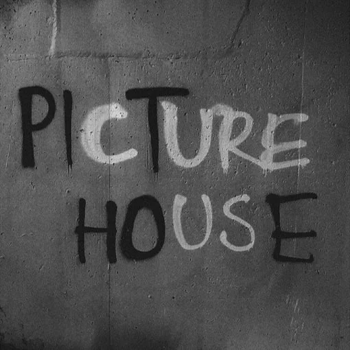 Graffiti on a brick wall spelling 'PICTURE HOUSE' with black and white spray paint.