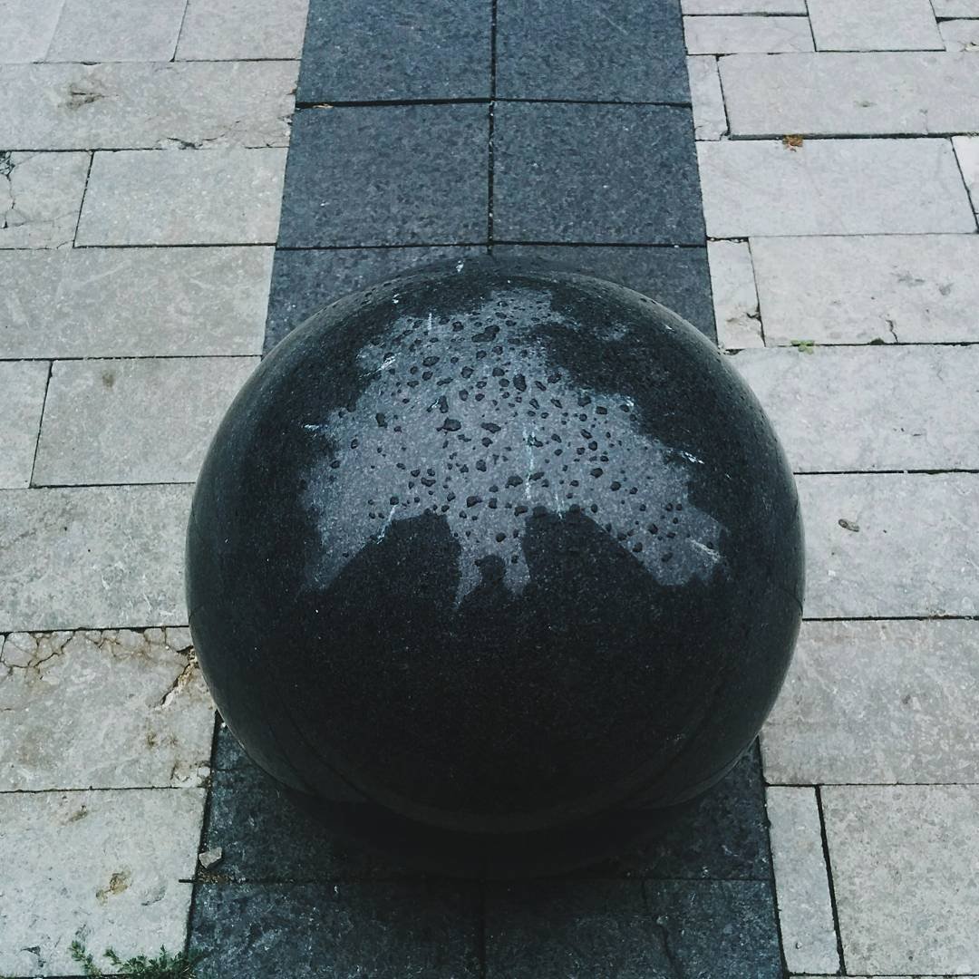 A large black spherical sculpture on a sidewalk with gray and beige paving stones.