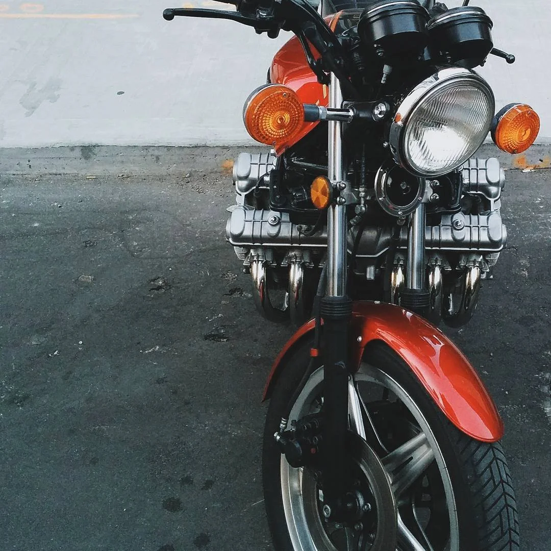 A red motorcycle parked on a paved surface with a white wall in the background.