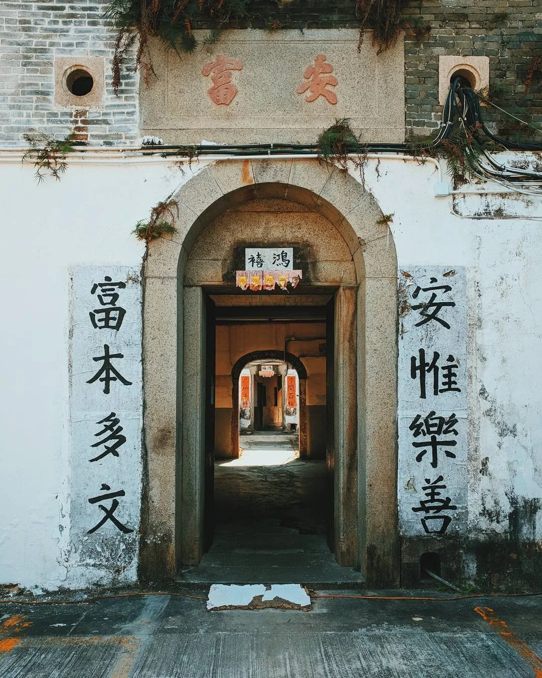 Traditional Chinese building entrance with stone archway and Chinese characters painted on the walls, leading to inner courtyards.
