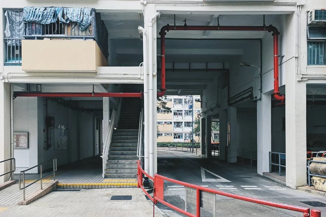 Underground parking garage with entry and exit lanes, visible stairs, and residential buildings in the background.