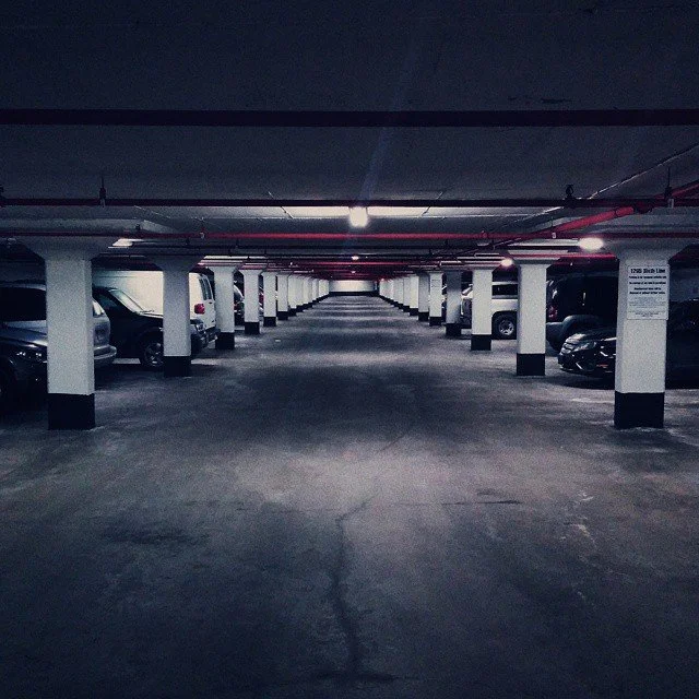 Underground parking garage with empty concrete floor, white columns, and parked cars along the sides.