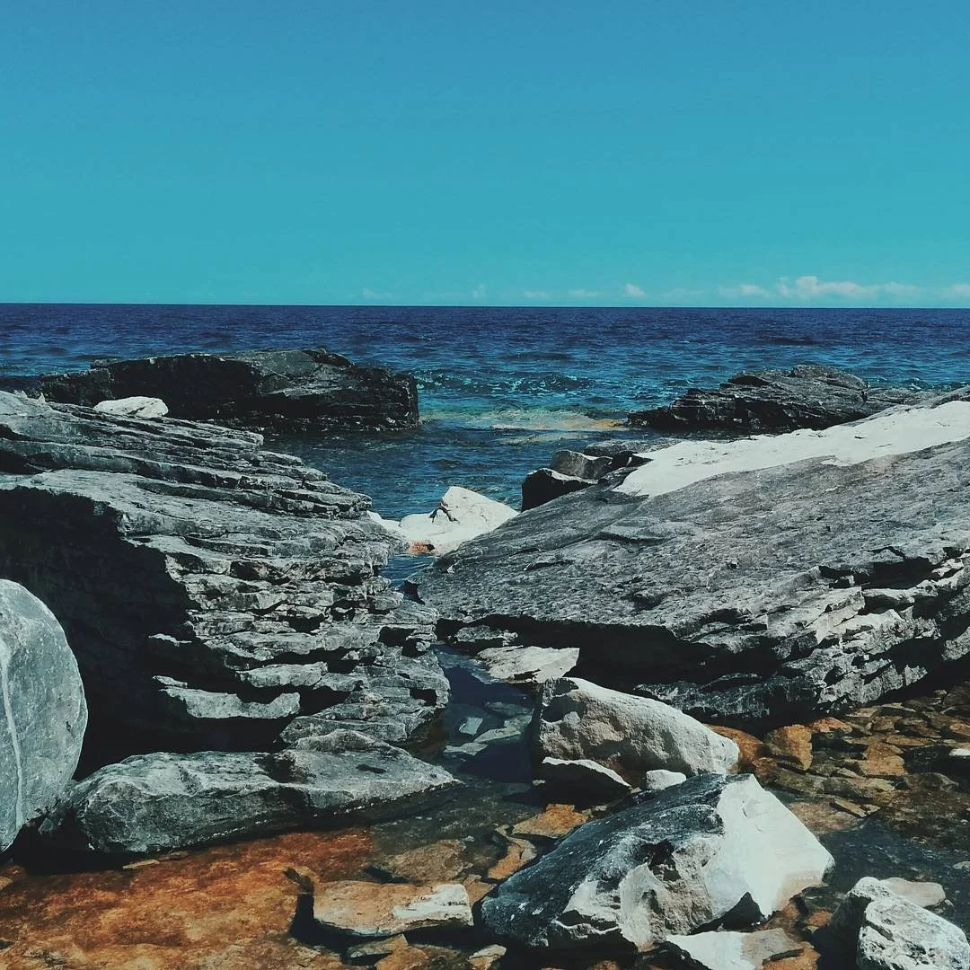 View of the ocean with blue sky and rocky shoreline in the foreground.