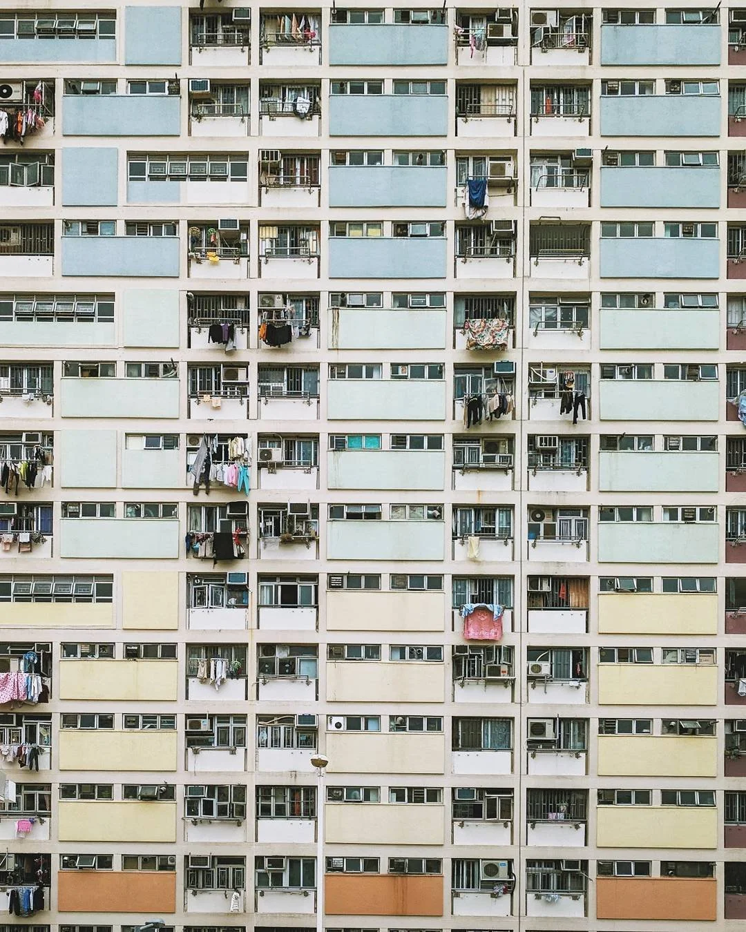 Apartment building with multiple balconies, some with laundry hanging, air conditioning units, and colored wall panels.