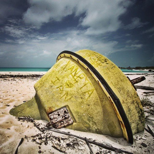 A large, yellow, weathered buoy lying on a sandy beach near the ocean, with a cloudy sky overhead.