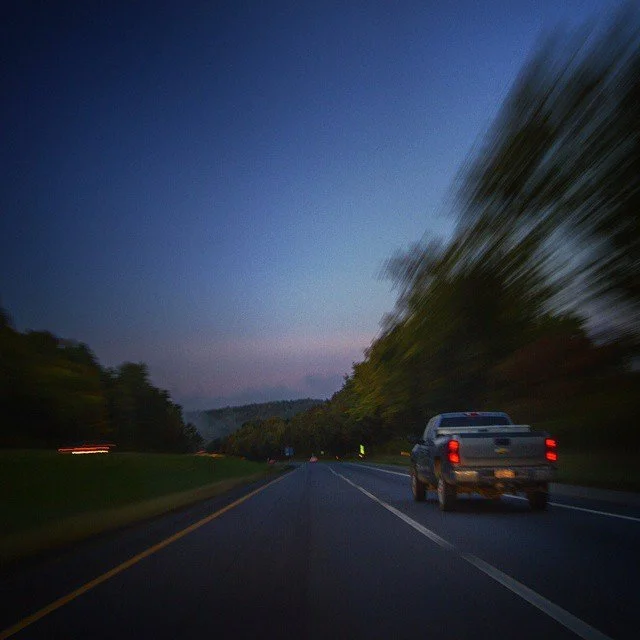 A moving vehicle on a highway at dusk with blurred trees on the sides.