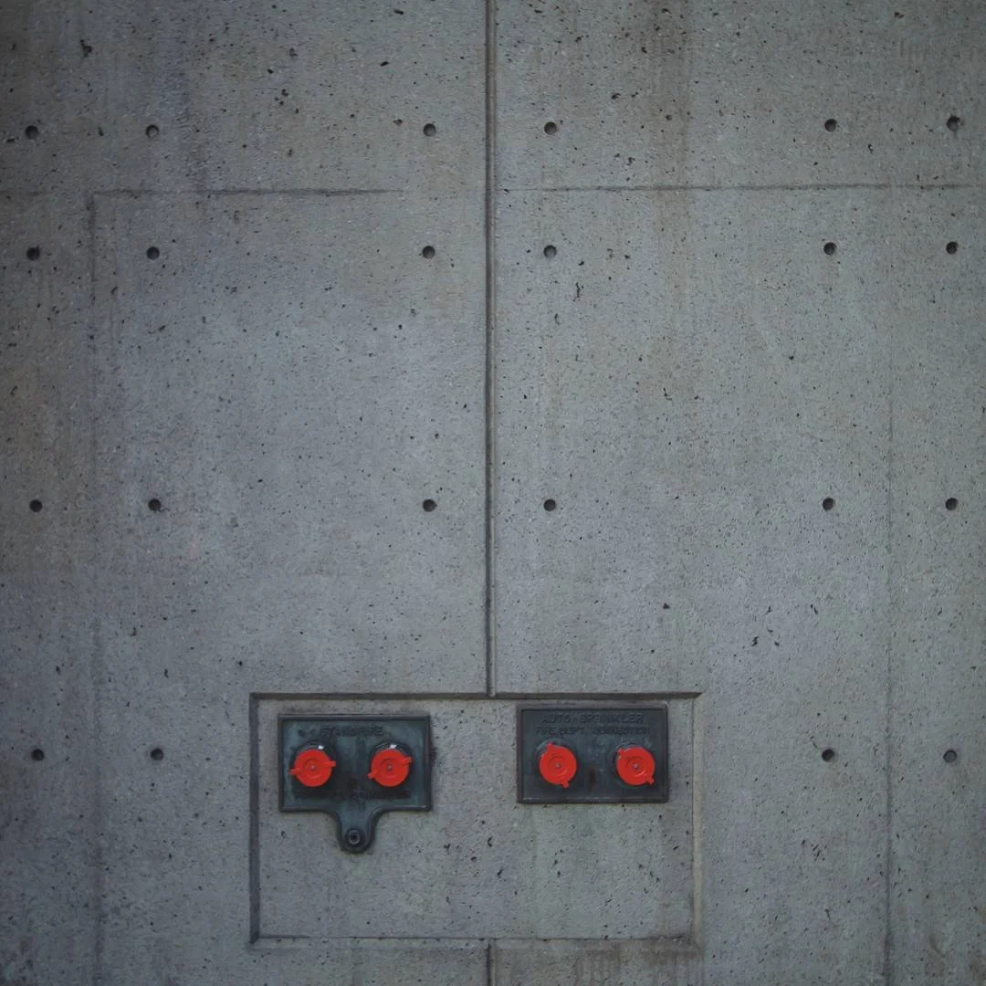 Concrete wall with two metal panels featuring red fire alarm switches.