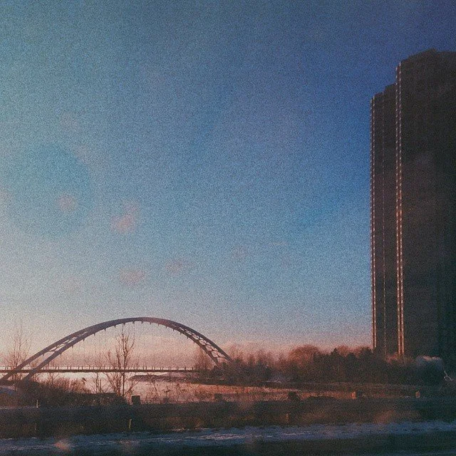 A cityscape at dusk with a bridge over a body of water and a tall building on the right