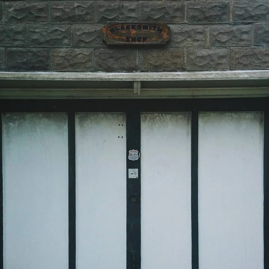 Garage door with a sign above that reads 'Blacksmith Shop' on a brick wall exterior.
