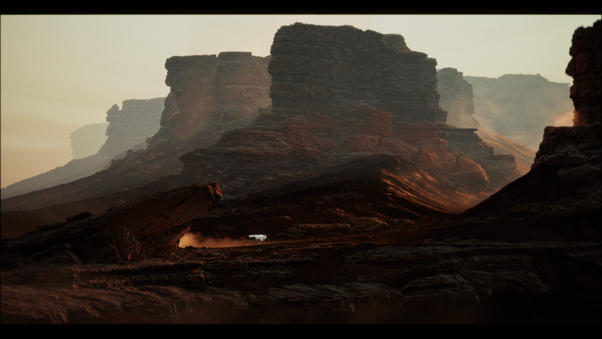 A vast desert landscape with tall, layered red rock formations at sunset and a white vehicle in the distance.