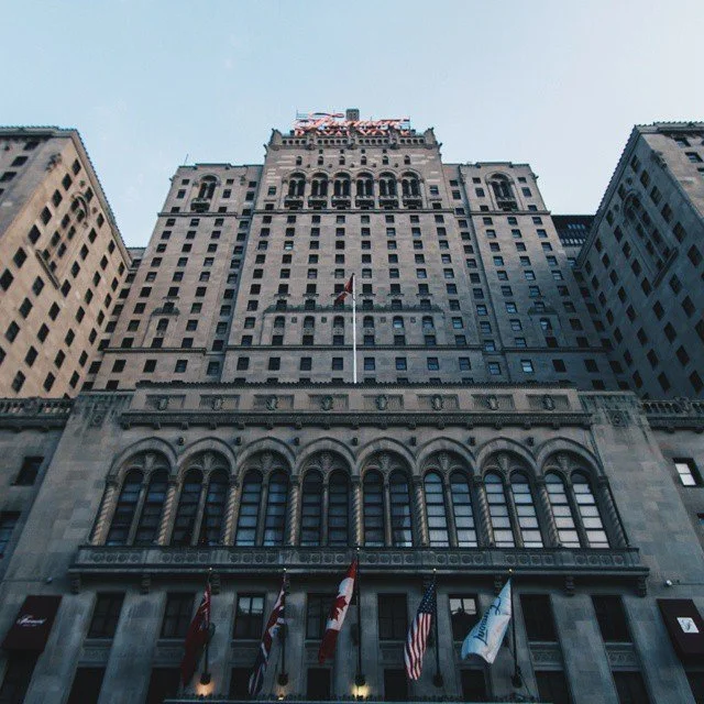 Tall historic building with multiple flags at the base, viewed from below, against a clear sky.